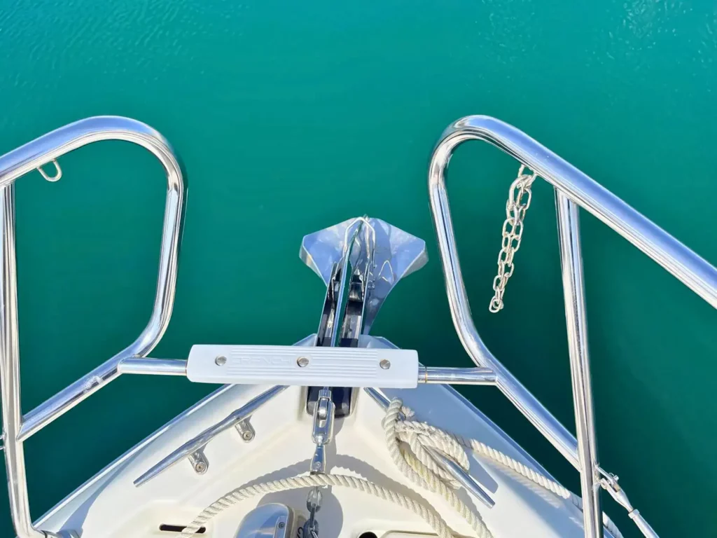 Blick vom Bug einer Cranchi T36 Yacht nach achtern, mit klarem türkisfarbenem Wasser durch die Geländer sichtbar, fokussiert auf den glänzenden Ankermechanismus.