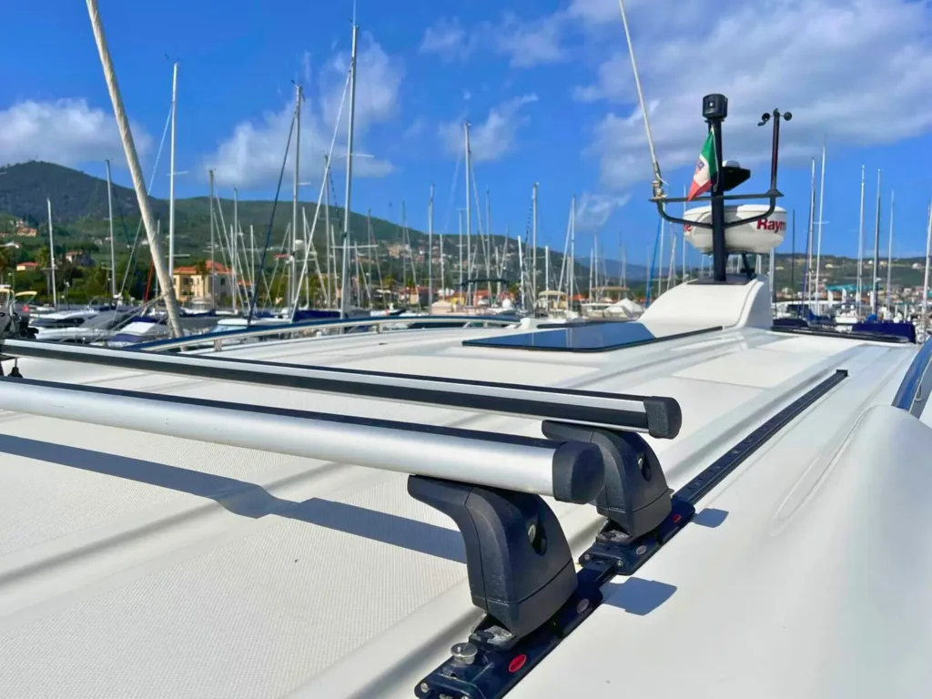 Nahaufnahme der Decksausrüstung auf einer Cranchi T36 Yacht, einschließlich Winden und Seilen, mit einem malerischen Hafen und grünen Hügeln im Hintergrund.