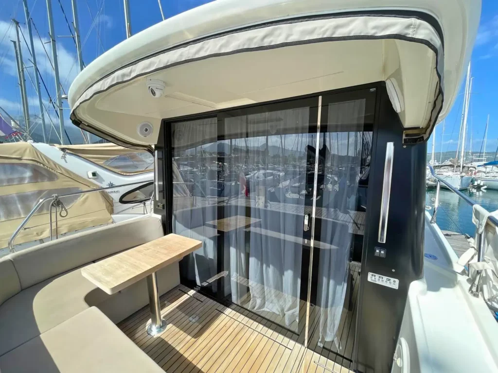 Heckbereich im Freien einer Cranchi T36 Yacht mit einem Sonnendach, einem Holztisch und transparenten Türen, die zum Innenraum führen.