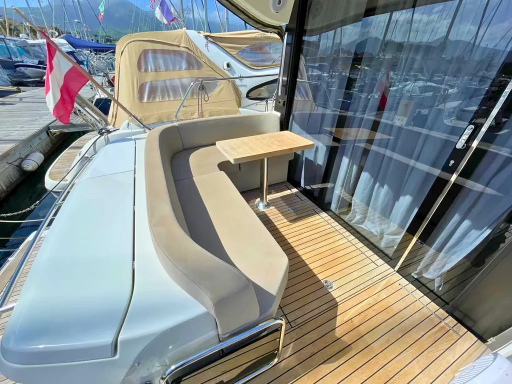 Außensitzplätze auf dem Achterdeck einer Cranchi T36 Yacht mit einer beigen Bank, einem Holztisch und sichtbarem Yachthafen im Hintergrund.