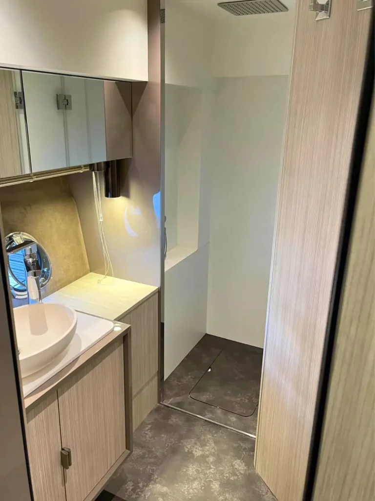 Innenraum des Badezimmers einer Cranchi T36 Yacht mit einem weißen Becken, einem verspiegelten Schrank und einer kompakten Duschkabine mit Glastür.