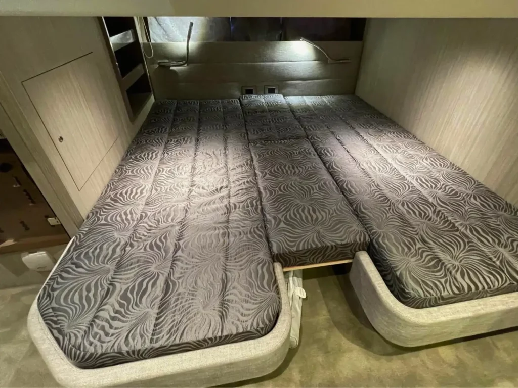 Schlafbereich in einer Cranchi T36 Yacht mit Zwillingsbetten in grau gemusterter Bettwäsche, Umgebungsbeleuchtung und holzverkleideten Wänden.