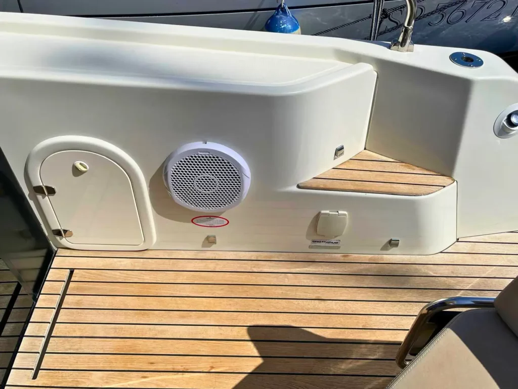 Detaillierte Ansicht des Achterdecks einer Cranchi T36 Yacht, die einen Lautsprecher, Stufen und einen Abschnitt des Holzbodens zeigt, wobei das Sonnenlicht Schatten wirft.