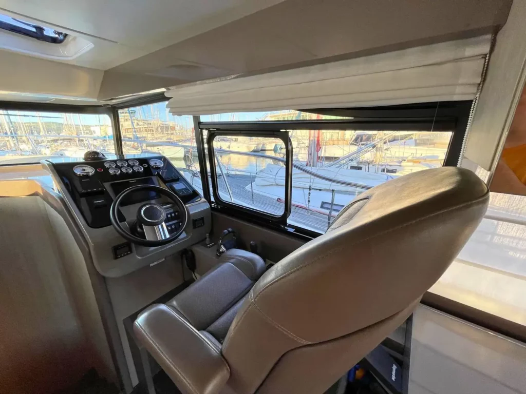 Cockpit einer Cranchi T36 Yacht mit einem modernen Bedienfeld mit mehreren Anzeigen und einem Ledersitz des Kapitäns, mit Blick auf den Yachthafen durch das Fenster.