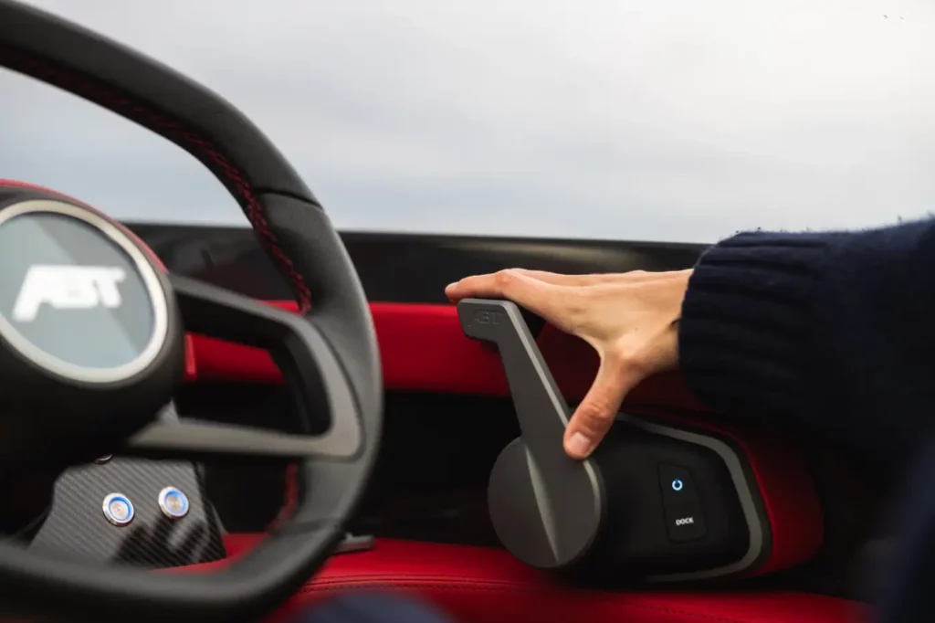 Detailansicht des Lenkrads und des Steuerhebels in der ABT Marian M 800-R, gezeigt wird eine Hand, die den Schalthebel ergreift. Das rote und schwarze Interieur, kombiniert mit Carbon-Akzenten, verleiht ein luxuriöses und modernes Ambiente.