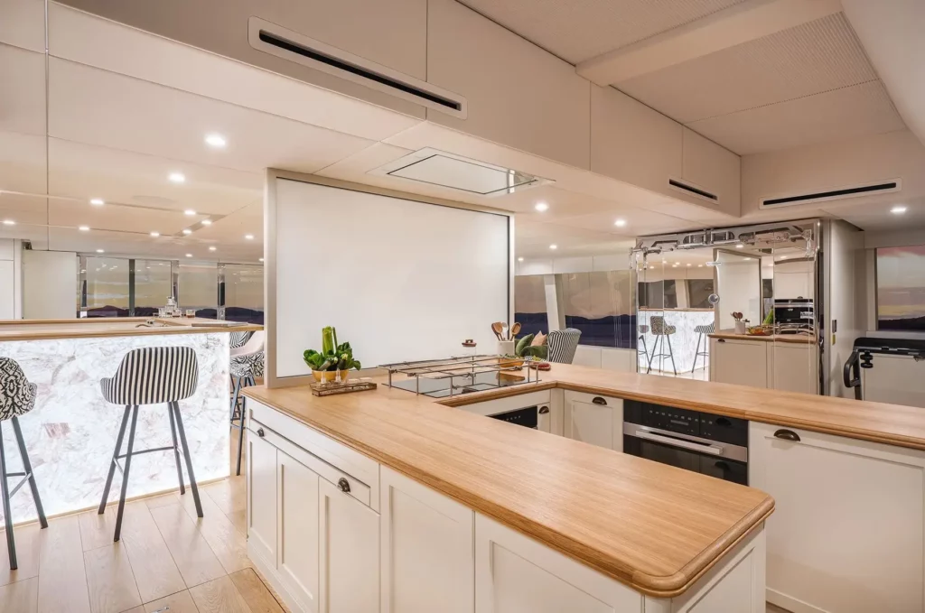 A modern and stylish kitchen on the 100 Sunreef Power yacht, with wooden countertops, white cabinetry, and a lighted bar area with striped bar stools.