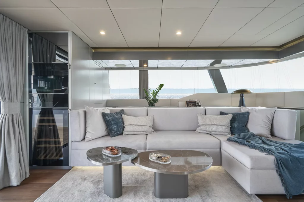 Stilvoller Wohnbereich auf der Sunreef 60, ausgestattet mit einem bequemen Sofa, Couchtisch und großen Fenstern mit Blick auf den Ozean.