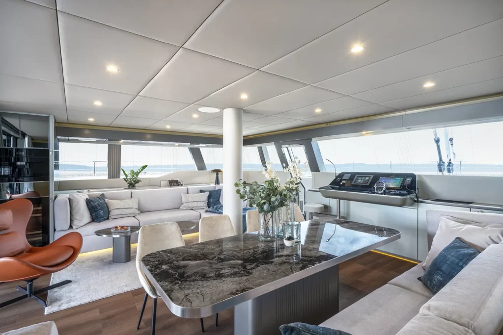 A spacious dining area on the Sunreef 60 yacht, with a large marble dining table, comfortable chairs, and a modern design. The area is well-lit, with large windows allowing natural light to fill the space.