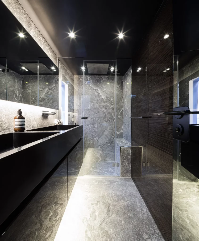 Hochmodernes Badezimmer auf der Sunreef 70 Yacht mit edlen Marmorböden und Wänden, einer gläsernen Dusche und stilvollen, dunklen Armaturen.