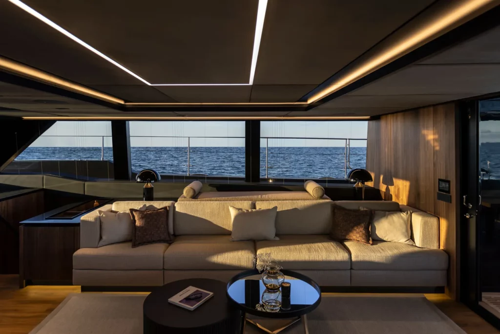 Der luxuriöse Salon des 70 Sunreef Power mit einer großen Couch, stilvollen Lampen und Panoramafenstern, die einen beeindruckenden Blick auf das Meer bieten.