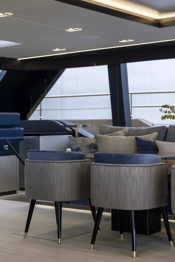 Nahaufnahme des stilvollen Sitzbereichs im Inneren der 80 Sunreef Power Yacht, mit komfortablen, gepolsterten Stühlen in einer neutralen Farbpalette, vor dem Hintergrund des eleganten, modernen Innendesigns der Yacht.