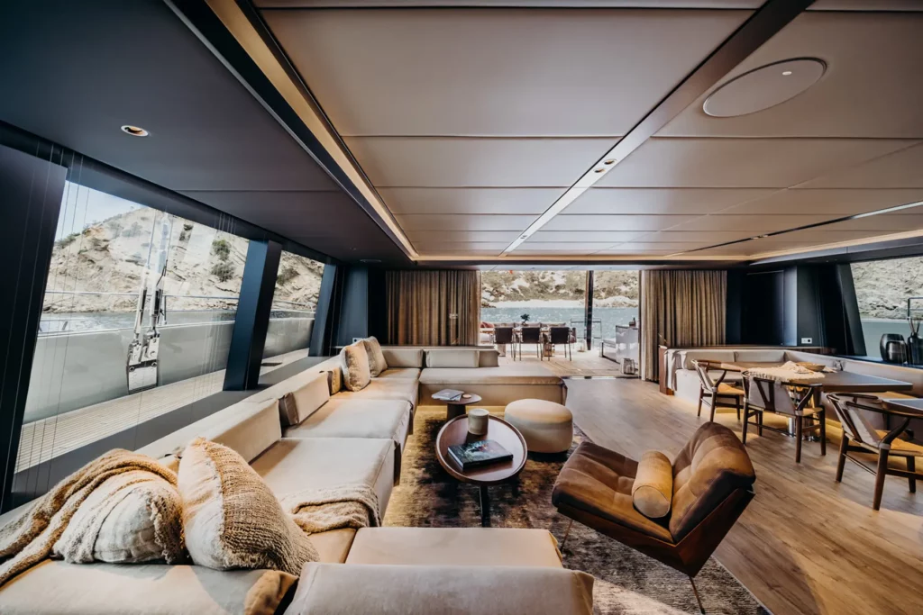 Weitläufiger Wohnbereich im Salon des Sunreef 80 Katamarans, mit großen Panoramafenstern, bequemen Sofas und einem Essbereich, der zu einer offenen Terrasse führt.