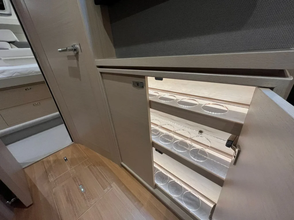 Innenaufnahme einer luxuriösen Yacht mit einem geöffneten Schrank, der speziell für Gläser entworfen wurde, mit beleuchteten Regalen. Perfekt abgestimmt auf das moderne Design der Princess V40 2022.