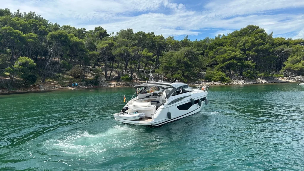 Die Princess V40 2022 in Bewegung auf einem ruhigen, türkisfarbenen Gewässer vor einer bewaldeten Küstenlandschaft. Ein perfektes Beispiel für luxuriöse Mobilität.