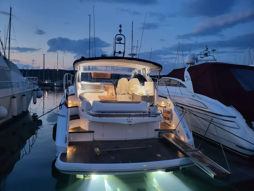 Rückansicht der Princess V40 2022 in einem Hafen, mit stilvoll beleuchtetem Heckbereich am Abend. Die Yacht bietet moderne Eleganz bei Tag und Nacht.